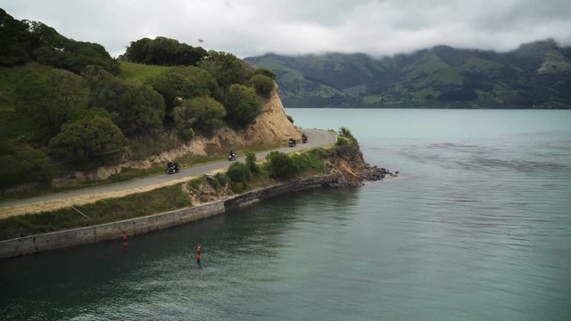 Drone shot motorcycle gang rides down road beside the coast