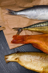 salted herring, smoked mackerel, perch and sig from Baikal on the paper bag in the black wooden background