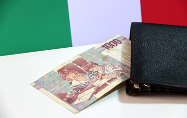 Fototapeta na wymiar One thousand Lire of Italy banknote with black wallet on the white floor with Italia flag background, Lire Italia money the concept of finance.