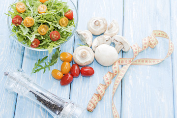 Health food. Fresh mushrooms and arugula salad, cherry tomatoes on light blue background. Diet meals.