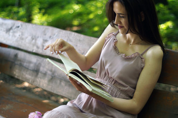 Pretty relaxed young beautiful woman reading a book on a bench with a shining sun. place for text