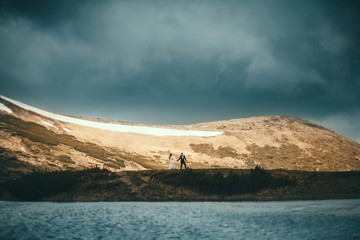 Scenic view of beautiful spring mountains and a lake. Wedding couple holding hands and walking on a hill. Beautiful landscape
