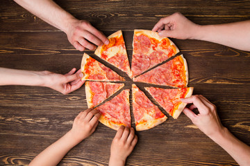 Hands taking pizza slices from wooden table, close up view
