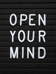 The words Open Your Mind in white plastic letters on a black letter board as an aid to learning and creativity
