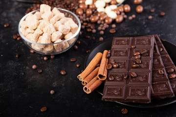 Chocolate tablets next to cinnamon rolls and other sweets and candies on a wooden background