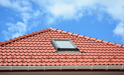 Beautiful ceramic tiled red  house roof  with roof gutter,  attic skylight window and copy space.
