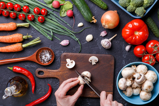 Picture on top of fresh vegetables, mushrooms, cutting board, oil, knife, hands of cook
