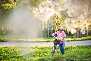 Beautiful senior woman with bicycle outside in spring nature.