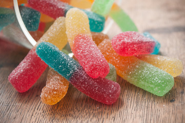 closeup of acidulous candies in shaped french fries falling from glass container on wooden background