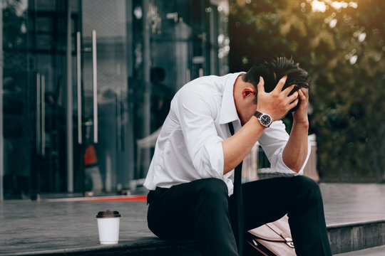 Asian young businessman stress sitting in front office with his hands covering his head against.