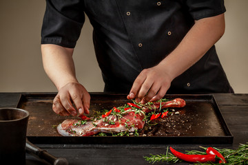 Male chef rubbing raw lamb shanks with greens and spices on stone tray on wooden table. Chef cooking appetizing shank of lamb. © nazarovsergey