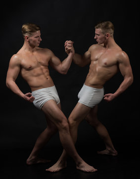 Twins men with muscular body in balance pose. twins muscular men in bodybuilder pose isolated on black background.