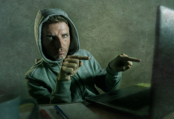 dangerous looking hacker man in hoodie hacking internet computer system pointing his eyes warning...