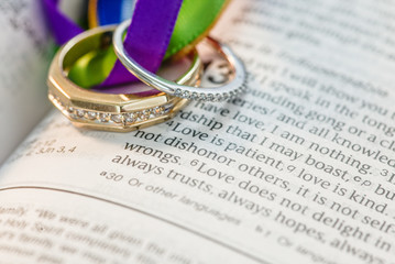 Wedding ring bands sitting on open book Holy Bible and colored ribbons