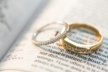 Wedding ring bands sitting on open book Holy Bible Love is patient phrase - obrazy, fototapety, plakaty