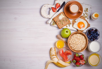Breakfast served with coffee, orange juice, oat cereal, milk, fruits, eggs and toast. Balanced diet. Morning sweet and savory meal, food background. overhead, horizontal