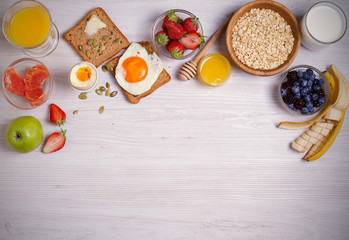 Breakfast served with coffee, orange juice, oat cereal, milk, fruits, eggs and toast. Balanced diet. Morning sweet and savory meal, food background. overhead, horizontal