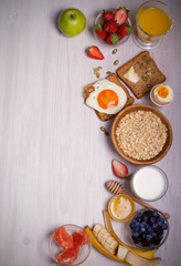 Breakfast served with coffee, orange juice, oat cereal, milk, fruits, eggs and toast. Balanced diet. Morning sweet and savory meal, food background. overhead, vertical