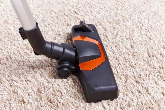 Crop piece of vacuum cleaner in work on top of soft textured carpet surface at home.