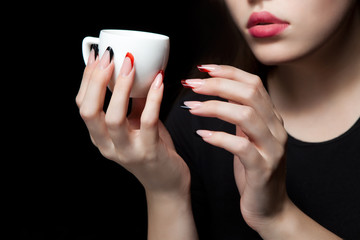Female hand with cup of coffee on black background.