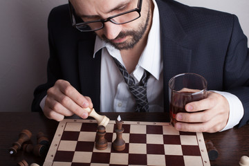 Business man playing chess and holds a glass of whiskey