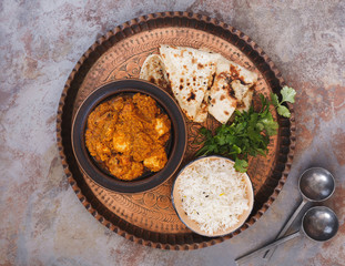 Indian curry dish chicken tikka masala with rice and naan bread on vintage copper tray. Top view, blank space, rustic background