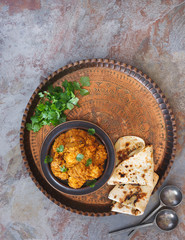 Chicken tikka masala, prepared with tandoori chicken, cooked in a sauce of tomato, yogurt and masala spices. Served with naan bread on vintage copper tray. Top view, blank space