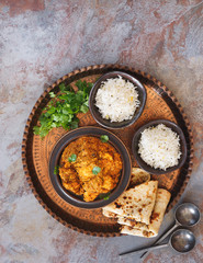 Chicken tikka masala, Indian chicken curry dish, served with naan bread and pilau rice on vintage copper tray, garnished with cilantro. Top view, blank space