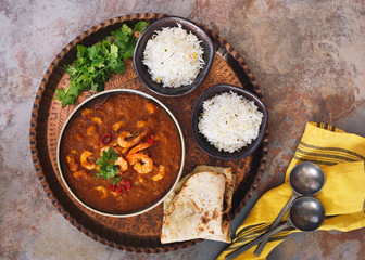 Curry shrimp. Spicy mixture of tomato and masala spices with shrimp. Served with naan bread and pilau rice on vintage copper tray. Top view, blank space