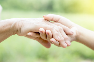 close-up of a daughter holding her mother's hand over nature green background