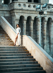 Young woman in white long dress stepping up staircase