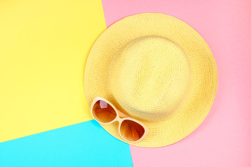 Hat, sunglasses on a three-color pastel background of blue, yellow and pink.