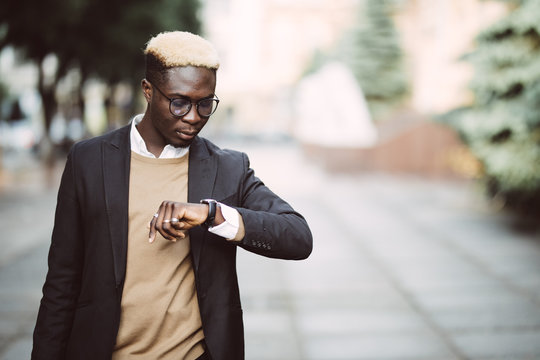 Handsome Afro American man looking at watch wearing suit in modern city street