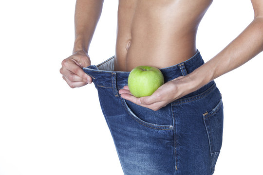 Thin girl in jeans with an apple in her hand on a white background. Weight loss concept