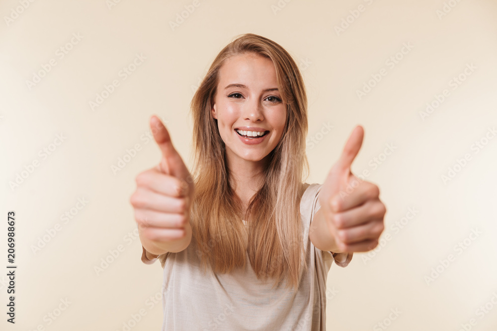 Sticker Image closeup of joyful caucasian woman wearing casual clothing smiling and showing thumbs up meaning good result or choice, isolated over beige background in studio