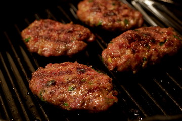 Four meat balls frying on cast iron skillet. Black background.