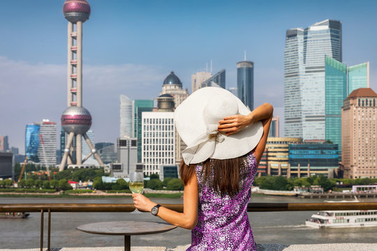 Attraktive Frau mit Sonnenhut genießt ein Glas Wein vor der Skyline von Shanghai, China