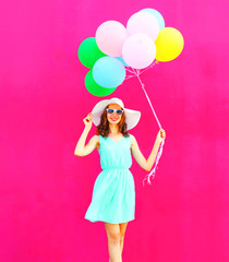 Cool girl with an air colorful balloons is walking over a pink background