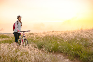 Young Woman Riding Mountain Bikes in the Beautiful Field of Feather Grass at Sunset. Adventure and Travel.