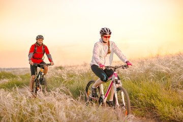 Fototapeta na wymiar Young Couple Riding Mountain Bikes in the Beautiful Field of Feather Grass at Sunset. Adventure and Family Travel.