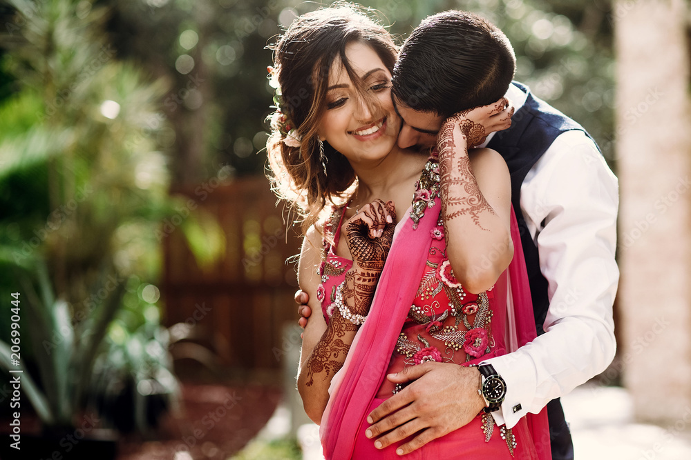 Wall mural hindu groom kisses bride in a sari tender standing in the morning park