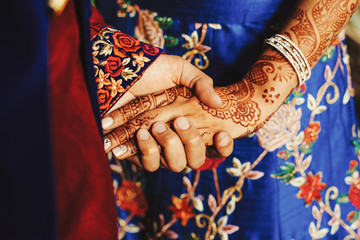 Hindu groom holds bride's hand covered with henna tattoos