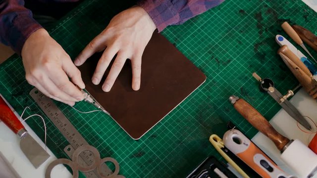 The master cuts the edge of the skin. A person performs one-handed action. Top view. The full cycle of production traveled a case of genuine leather. Handmade.