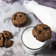 Chocolate biscuits next to a glass bottle and a glass of milk on a gray table. Top view, flat lay