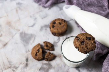 Chocolate biscuits next to a glass bottle and a glass of milk on a gray table. Top view, flat lay