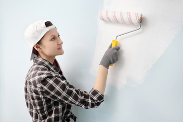 Girl painter, designer and worker paints a roller and brush the wall. Smiling, working with pleasure, close-up.