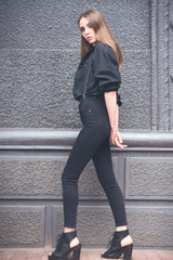 Beautiful girl in black clothes oversize with suspenders. Dark background. Toned image.