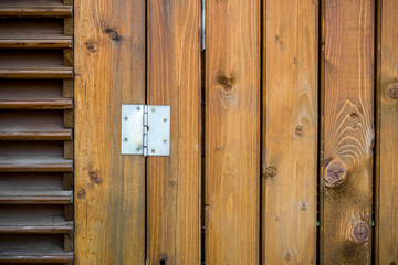 Wooden door made of vertical wooden planks with shiny metal hinge 