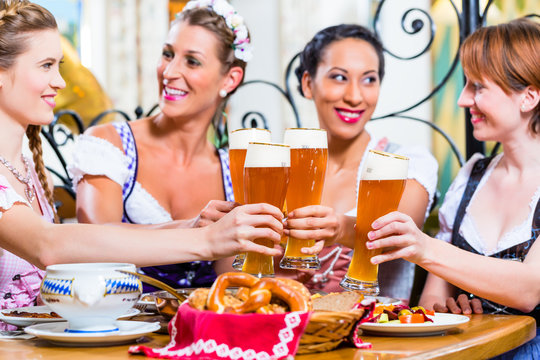 Girls toasting with wheat beer in Bavarian pub in front of pretzel