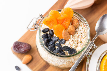 Healthy breakfast in glass mason jar with oat flakes, granola, milk, dry fruits and nuts, dates, honey, orange juice, eggs for morning fitness on wooden board platter on white background isolated